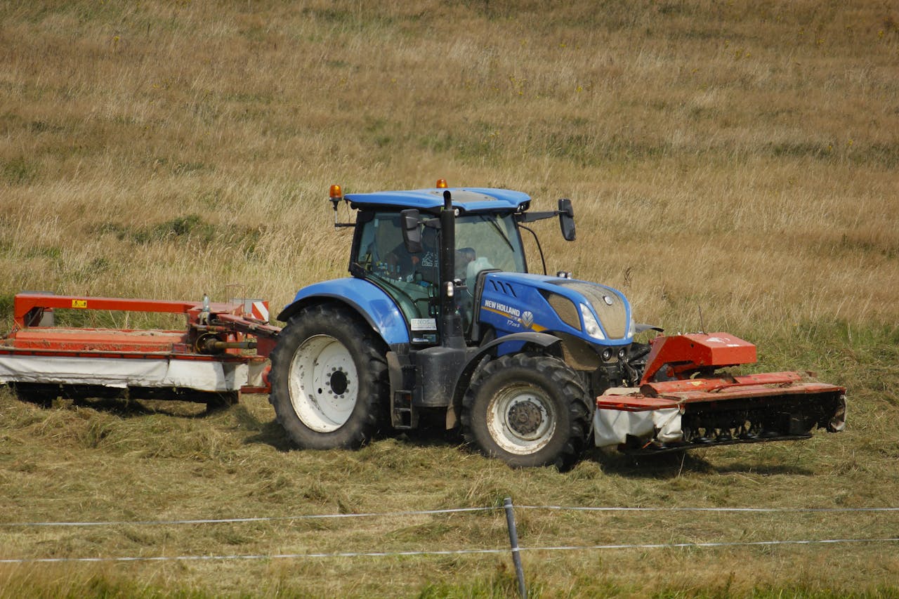 Blue tractor working in an open field during the day, harvesting crops in the countryside.