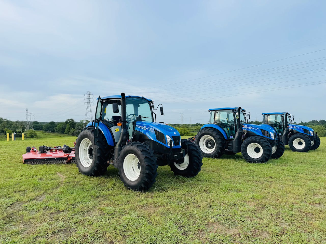 Three blue tractors parked in a Houston field against a clear sky, showcasing agricultural machinery.