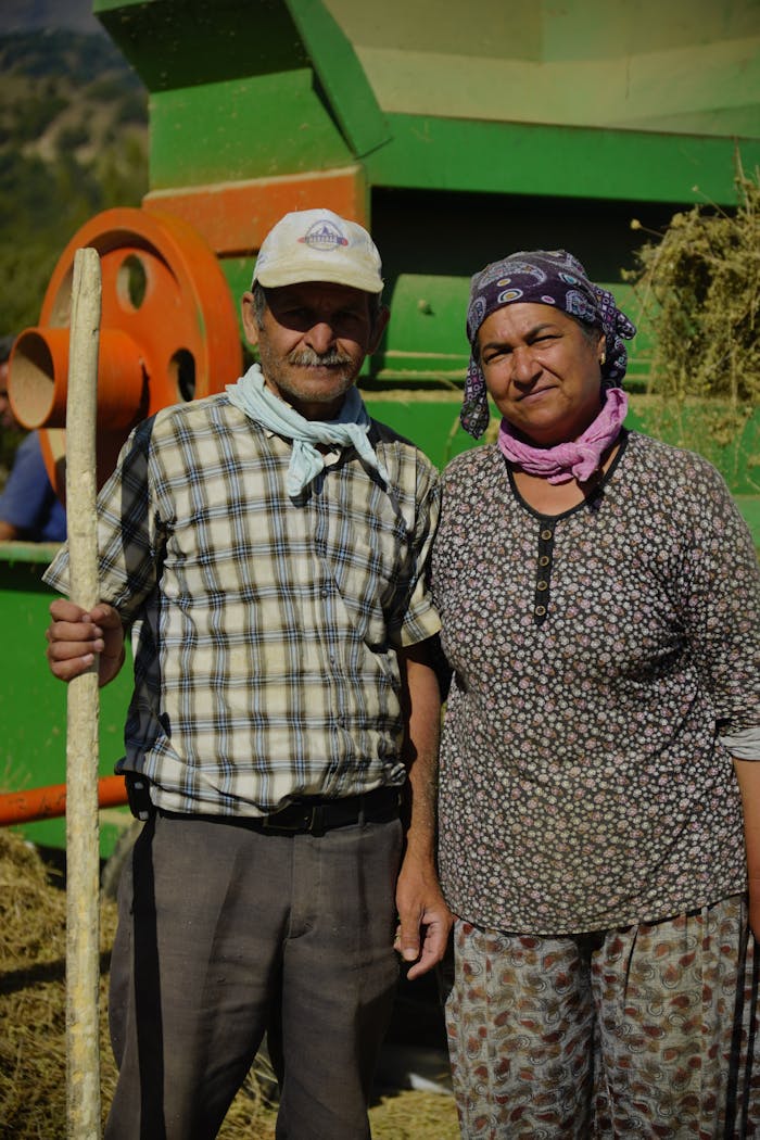 Portrait of farmers harvesting hay in Türkiye with farming machinery in background.